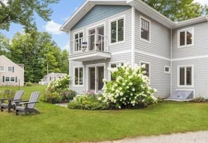 Ein zweistöckiges Haus mit Balkon, Veranda und gepflegtem Rasen.