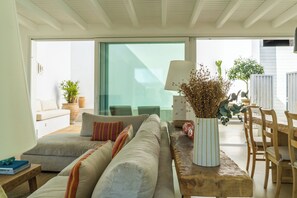 A modern living room with a sofa, a wooden table, and a dining area with chairs.