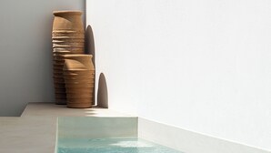 Una piscina con agua cristalina, una pared blanca y una pila de macetas de terracota.