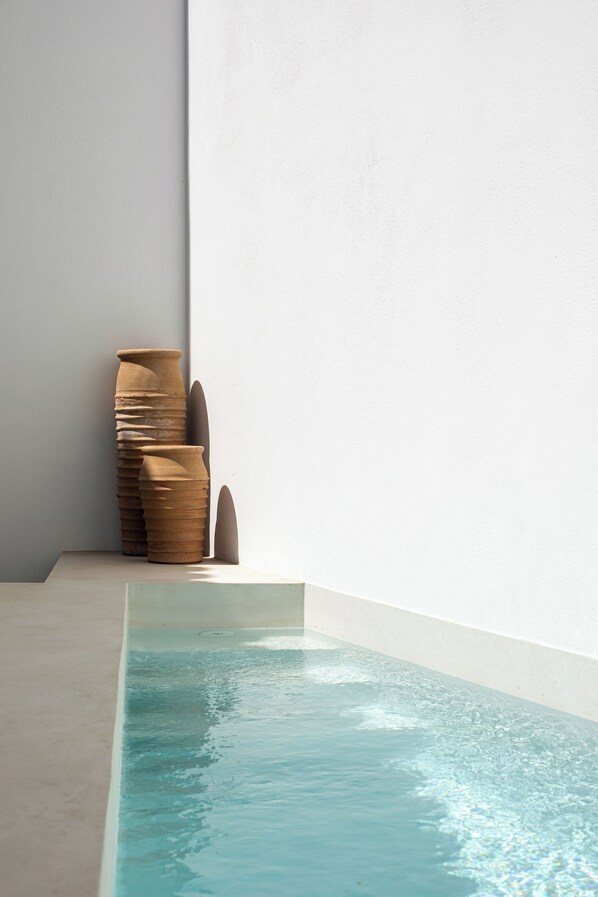 A pool with clear water, a white wall, and a stack of terracotta pots.
