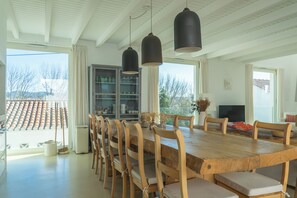 A spacious dining area with a large wooden table and chairs, pendant lighting, a view of the outside, and a built-in cabinet with glass doors.