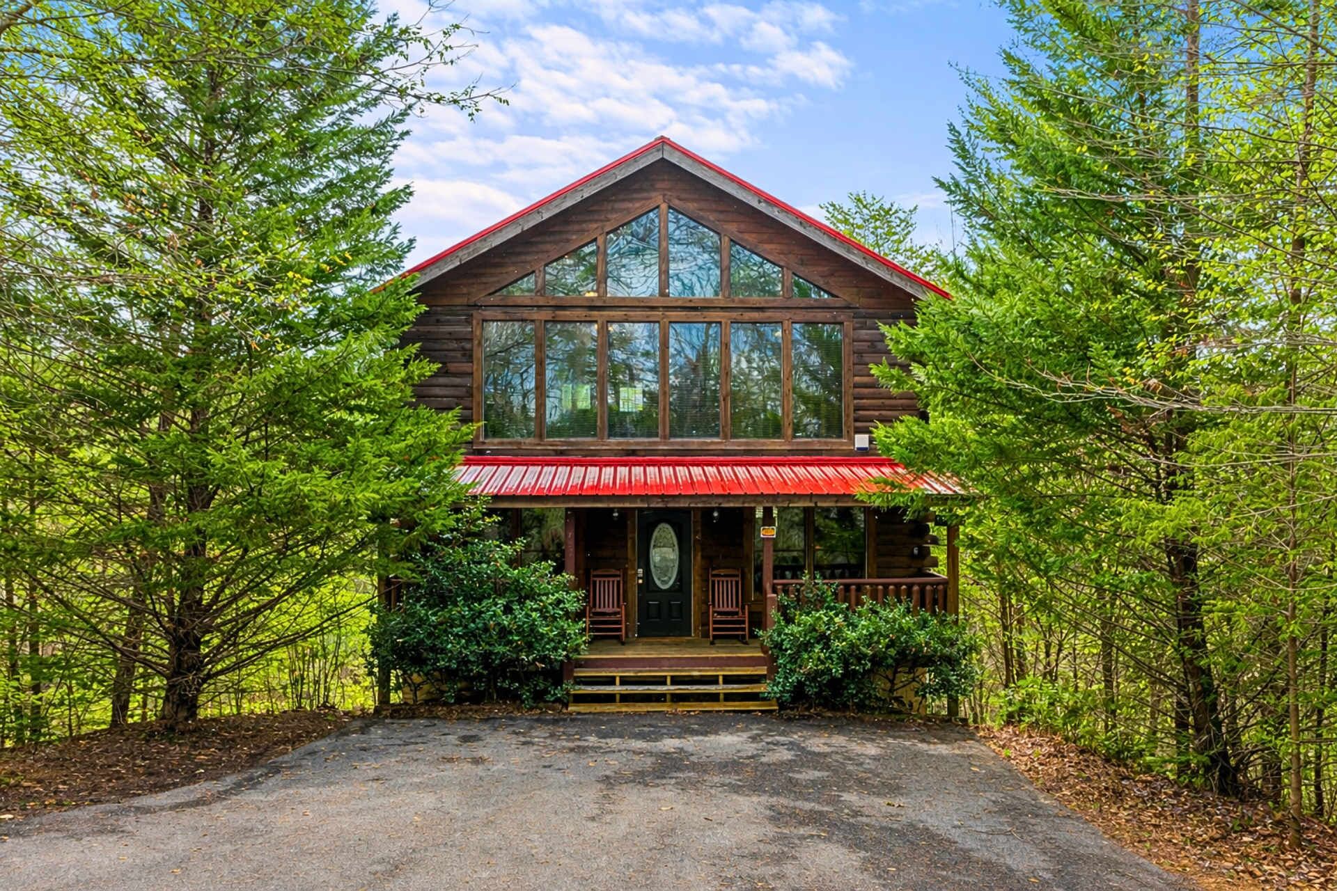 A log cabin with a red roof, large windows, and a porch with steps leading to the entrance.