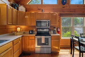 A cabin kitchen with wooden cabinets, a stainless steel oven, a microwave, and a window overlooking greenery. - Ridgecrest Retreat | Hot Tub • Decks • Game Room! (Gatlinburg)
