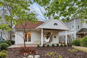 Ein eingeschossiges Haus mit überdachter Veranda, einem kleinen Gartenbereich mit Mulch und Pflanzen, und einem Baum im Vordergrund.