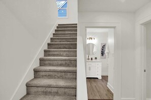 Eine Treppe führt zu einem Raum mit weißer Wand, kleinem Fenster und Holzboden.