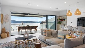 Un salon moderne doté d’une grande porte vitrée donnant sur un balcon qui offre une vue sur une étendue d’eau.