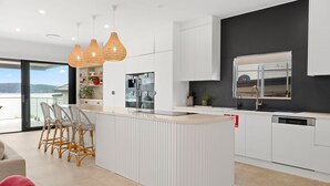 Une cuisine moderne dotée d’un îlot central, de luminaires suspendus et offrant une vue sur l’extérieur.
