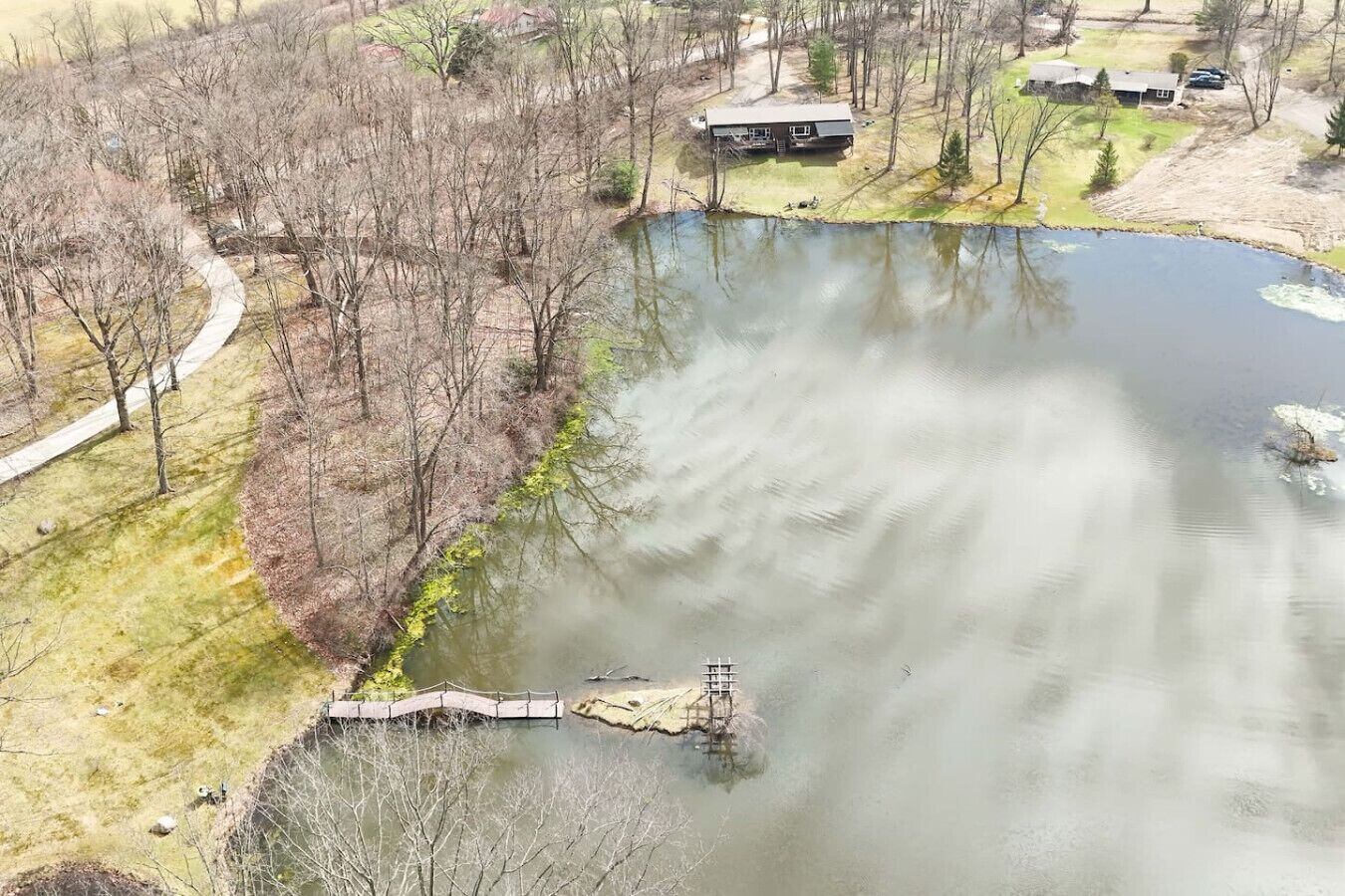A pond with a bridge, surrounded by trees and a building.