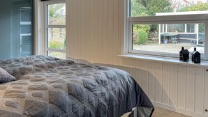 Ein Schlafzimmer mit einem Bett, einem Fenster mit Blick nach draußen und einer kleinen Ablage mit zwei Flaschen.