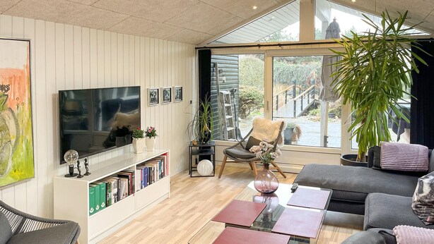 Ein modernes Wohnzimmer mit Flachbildfernseher, Bücherregalen, einer Couch, einem Glastisch und einem großen Fenster mit Blick auf einen Garten und eine Statue.
