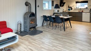Ein modernes Interieur mit Kaminofen, Essbereich mit Stühlen, Küche mit Geräte und ein rotes Sofa.