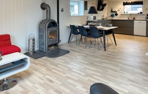 Ein modernes Interieur mit Kaminofen, Essbereich mit Stühlen, Küche mit Geräte und ein rotes Sofa.