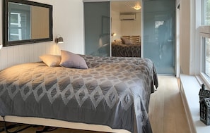 Ein Schlafzimmer mit einem Bett, einem Spiegel, einer Lampe und einer Glastür, die auf einen Balkon führt.