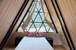 Ein raumförmiger Raum mit einem Bett, einem Fenster mit Vorhängen und Blick auf Grünfläche außerhalb.