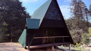 Eine dreieckige Holzhütte mit geneigtem Dach, umgeben von Bäumen.
