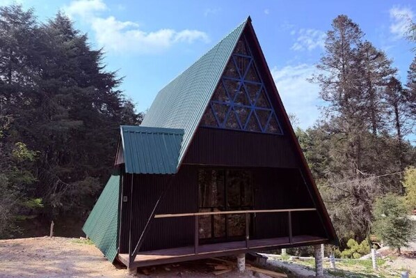 Eine dreieckige Holzhütte mit geneigtem Dach, umgeben von Bäumen.