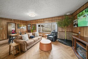 Una sala de estar acogedora con piso de madera, un sofá de cuero, una mesa de centro, una chimenea y un televisor montado en la pared.