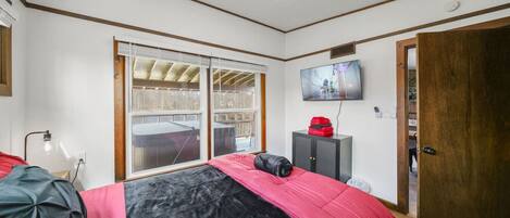 A bedroom with a bed, a TV, a window, and a door.
