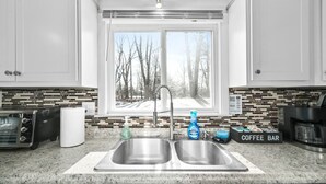 A kitchen with a double sink, a coffee bar, and a view of trees through the window. - Red Fox Run & Hawk`s Haven At Heron Hill Retreat! (Streetsboro)