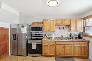 A kitchen with stainless steel appliances, wooden cabinets, a granite countertop, and a window with blinds.