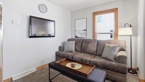 A living room with a sofa, a flat-screen TV, a lamp, and a tray with a cake. - The Appleton Downtown Den (Appleton)