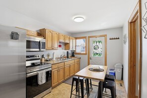A compact kitchen with wooden cabinets, stainless steel appliances, a small dining area, and a window with a view.