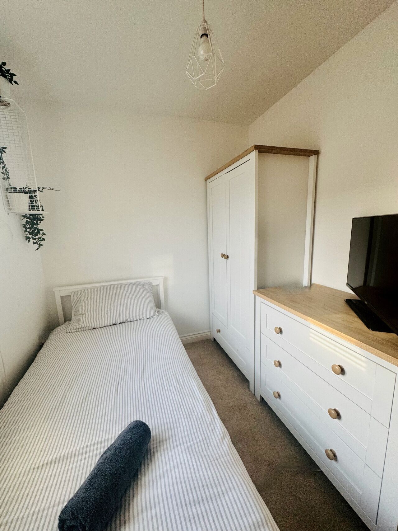 A bedroom with a bed, a wardrobe, a television, and a hanging light fixture.