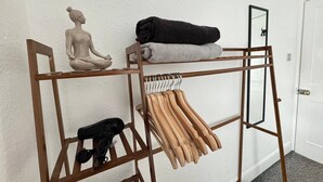 Un perchero de madera con toallas dobladas, perchas, una pequeña estatua y un espejo.