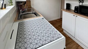 Una cocina compacta con muebles blancos, un salpicadero hexagonal, una lámpara colgante y un cartel en la pared que dice 'I CAME TO BOOGIE'.