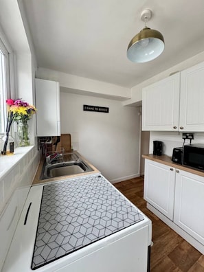 A compact kitchen with white cabinetry, a hexagonal backsplash, a hanging light fixture, and a 'I CAME TO BOOGIE' sign on the wall. - Compact, Quirky & Cosy Home in Central Exeter (Devon)