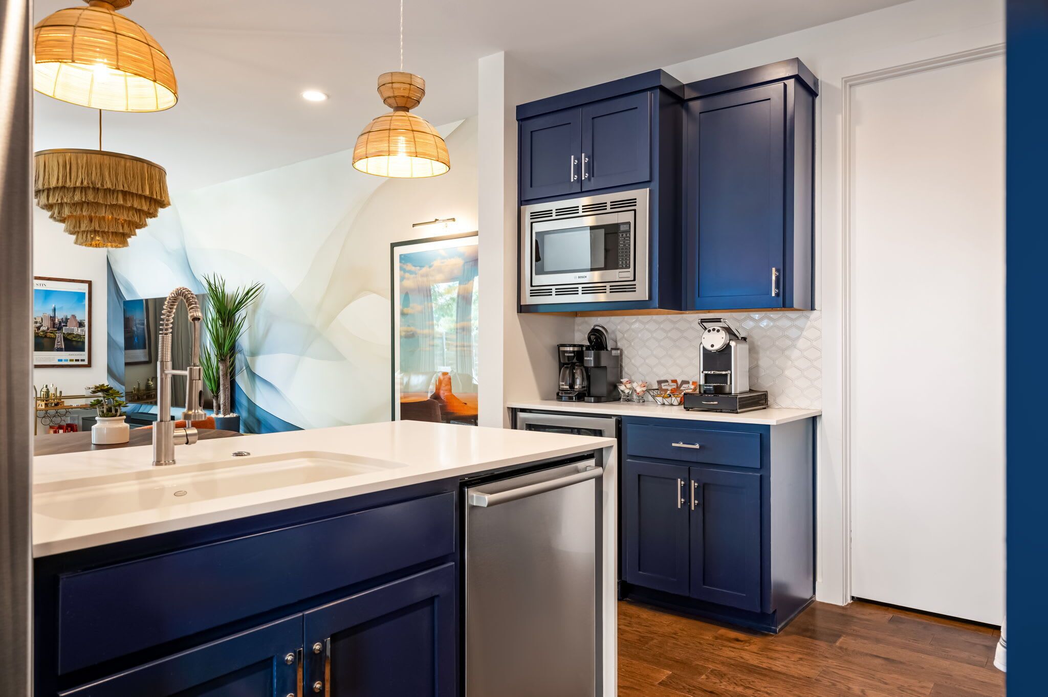 A modern kitchen with dark blue cabinets, stainless steel appliances, and pendant lighting.