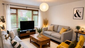 Ein Wohnzimmer mit Sofa, Sesseln, Couchtisch, Fernseher und einem Gemälde an der Wand.