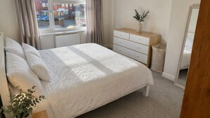 Ein Schlafzimmer mit einem großen Bett, einem Schminktisch, einem Spiegel, einem Fenster mit Vorhängen und einer Hängeleuchte.