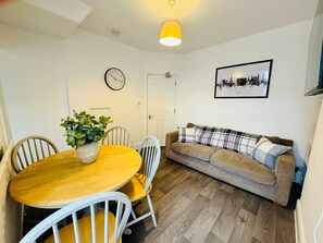 Ein Zimmer mit einem Holzesstisch, Stühlen, einer Couch, einer Uhr und einem gerahmten Bild an der Wand.