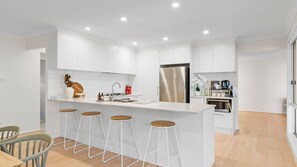 Une cuisine moderne avec des meubles blancs, un réfrigérateur en acier inoxydable et un îlot central doté de tabourets.