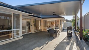 A covered patio with a table and chairs, a barbecue grill, and a view of the interior through glass doors. - The Hamlyn Terrace Hideaway - Hannah's Summer home (Hamlyn Terrace)