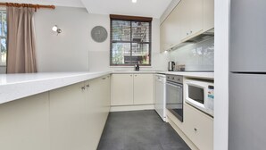 Una cocina compacta con encimera blanca, un reloj, una ventana con persianas y un horno empotrado.