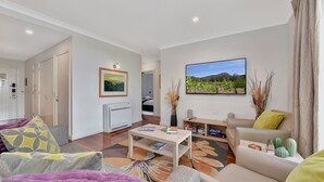 Una sala moderna con sofá, mesa de centro y televisor. Hay un cuadro en la pared y una puerta que da a otra habitación.