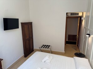 A hotel room with a bed, a television mounted on the wall, a wardrobe, and a door leading to another room. - Hotel Posta - Palazzo Guidoni (Orvieto)