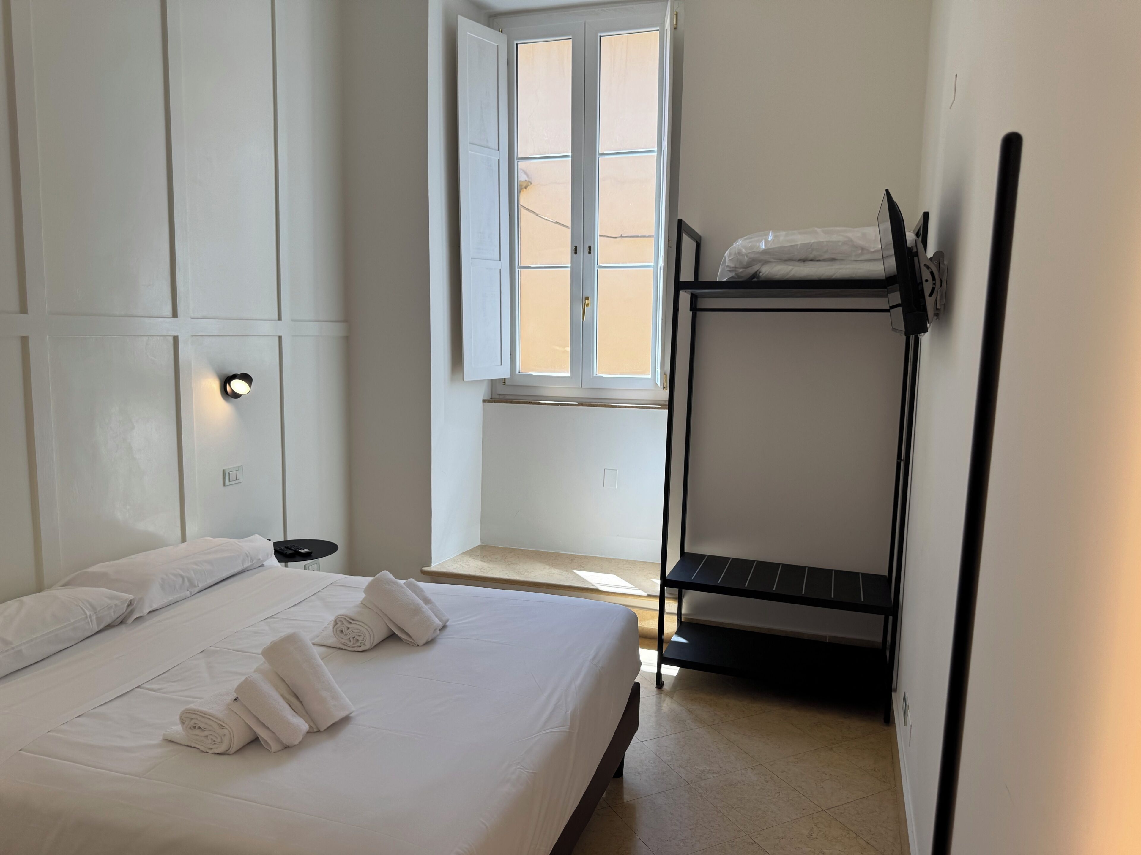 Una habitación de hotel con cama, ventana, mesita de noche y literas.