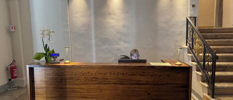 A reception desk with a wooden finish, a digital display, and a vase with white flowers.