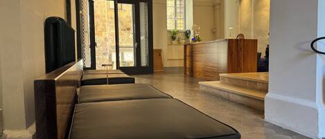 A hotel lobby with a reception desk, seating area, and a view of the outside through large doors.