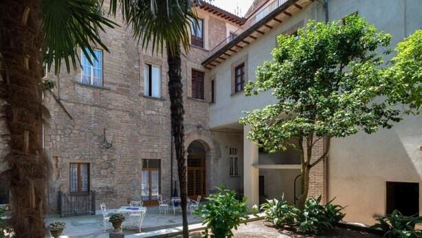 Un patio con edificios de piedra, una palmera y mobiliario exterior.