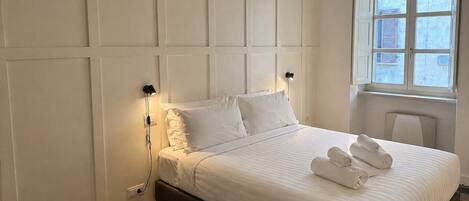 A bedroom with a bed, white walls, a window, and a radiator.