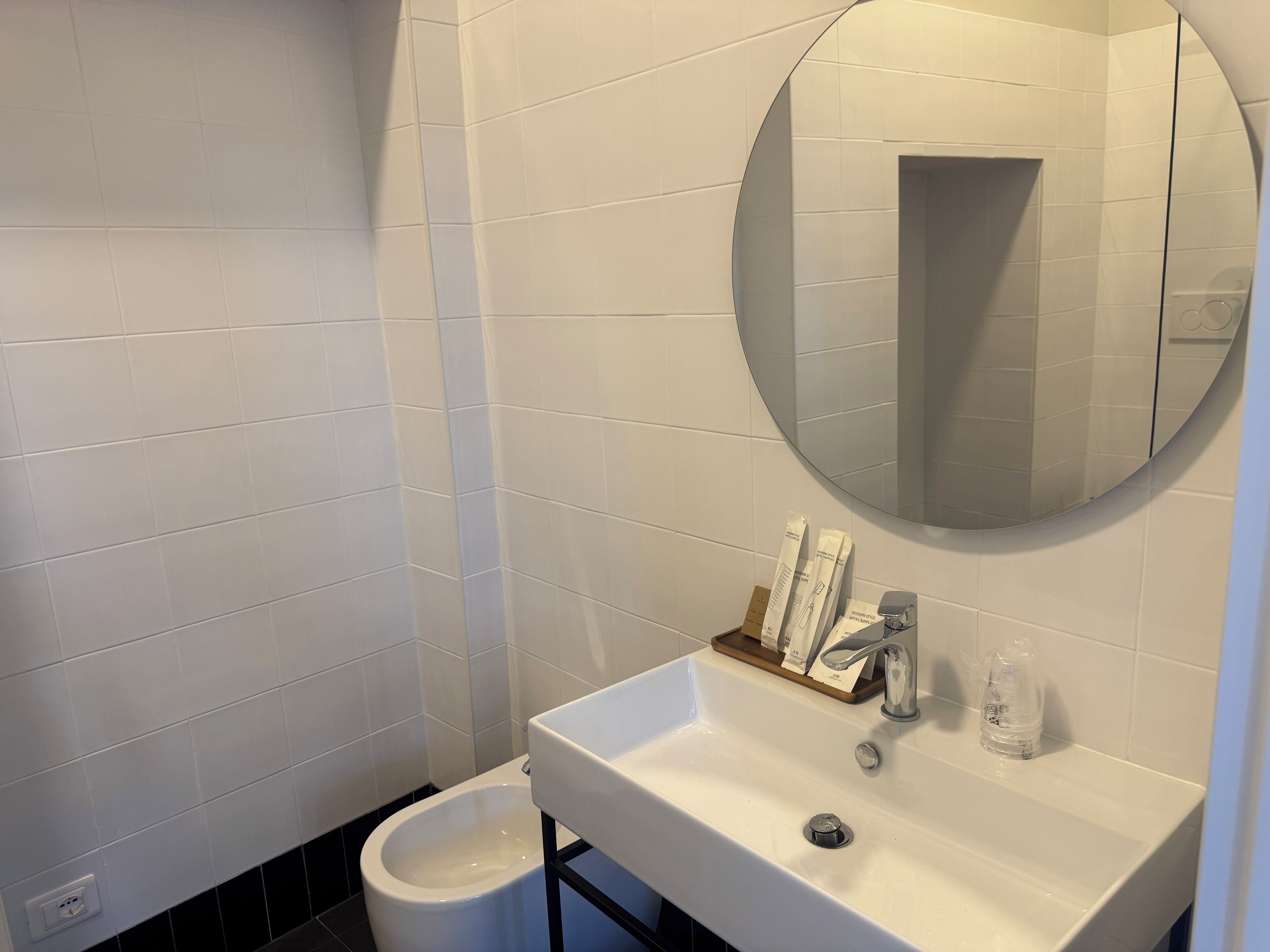 Un baño con un lavamanos blanco, un espejo y un inodoro negro.