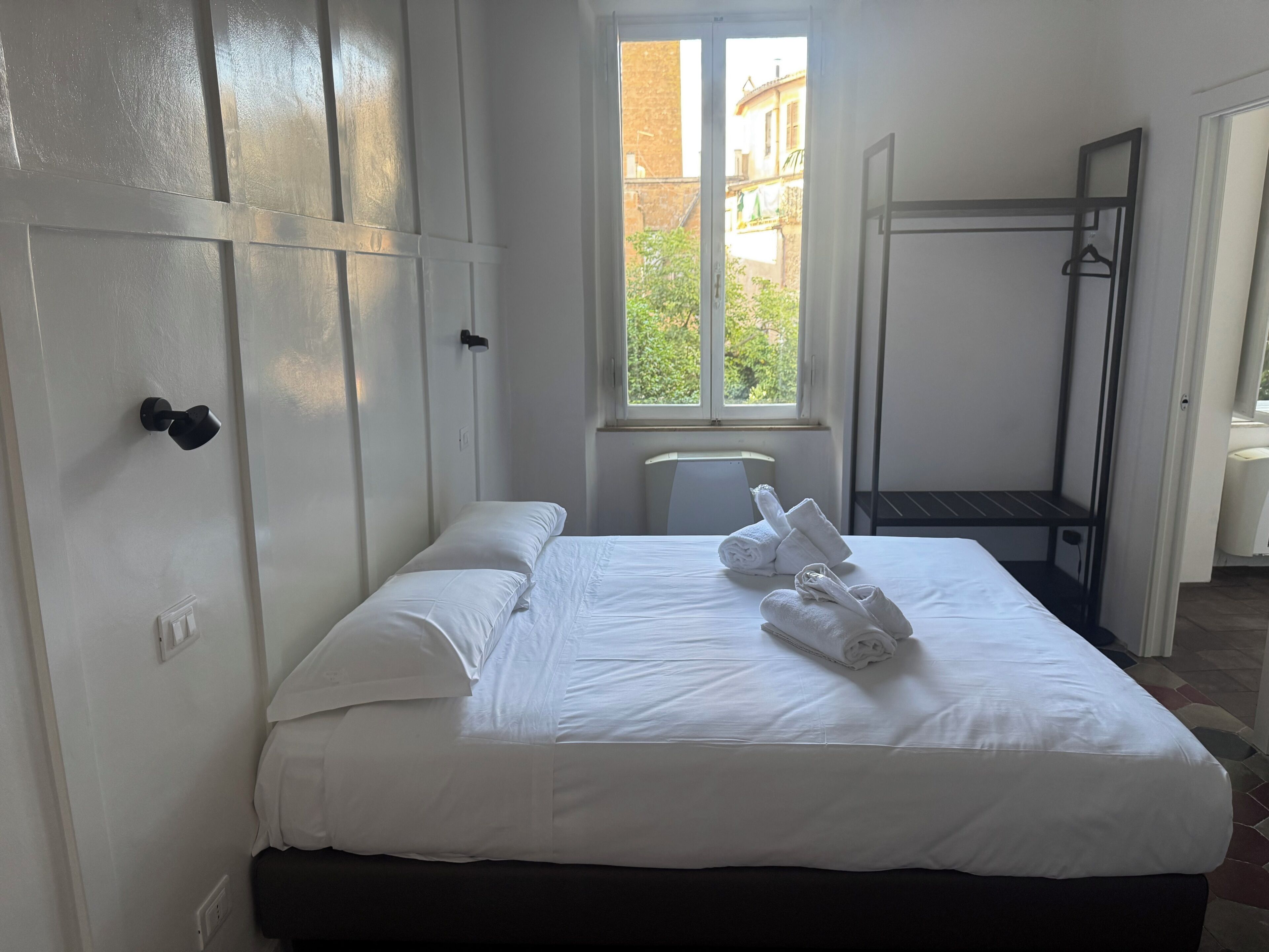 Ein Hotelzimmer mit Bett, Fenster, Handtuchhalter und Kleiderständer.