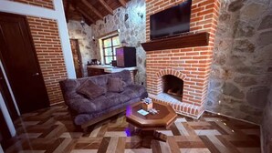 Ein gemütliches Wohnzimmer mit Kamin aus Backstein, einer bequemen Couch und einem darüber montierten Fernseher.