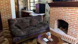 Ein Wohnzimmer mit einer Couch, einem Kamin, einem Fernseher und einer Küchenzeile im Hintergrund.