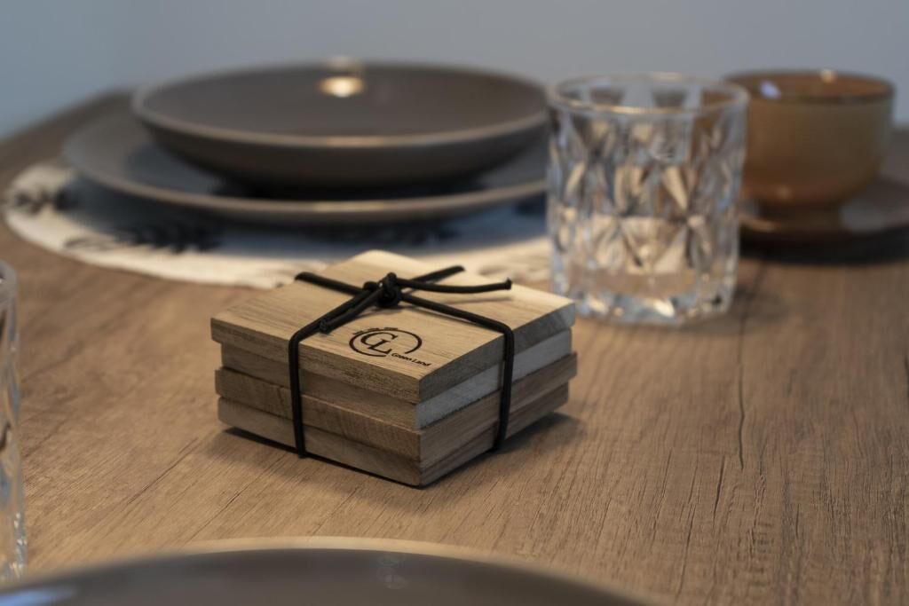 Una mesa de madera con una pila de bloques de madera atados con un cordón negro, un vaso con un diseño texturizado y una taza marrón sobre una bandeja.