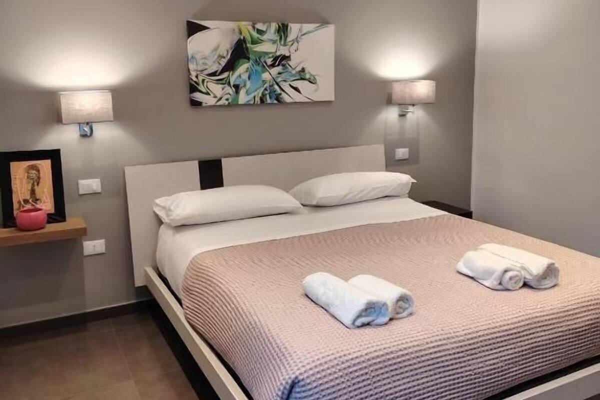 Een moderne slaapkamer met een bed, twee wandlampen, een schilderij en een klein plankje met een fotolijstje.